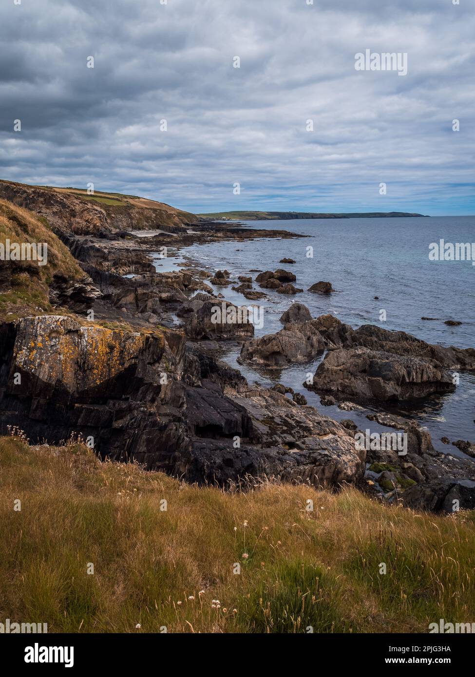 Picturesque landscape. Wild vegetation on stony soil. Cloudy sky over the ocean. Views on the wild Atlantic way, hills under clouds. Stock Photo
