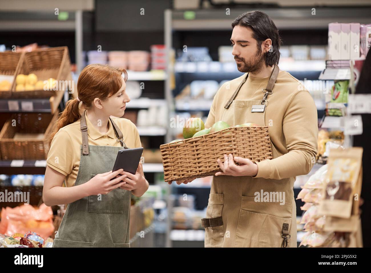 Waist up portrait of two young workers in supermarket stocking shelves with fresh fruit Stock