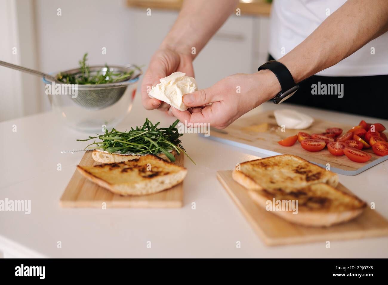 Human hand put piece of mozzarella on sandwich with arugula. Classic