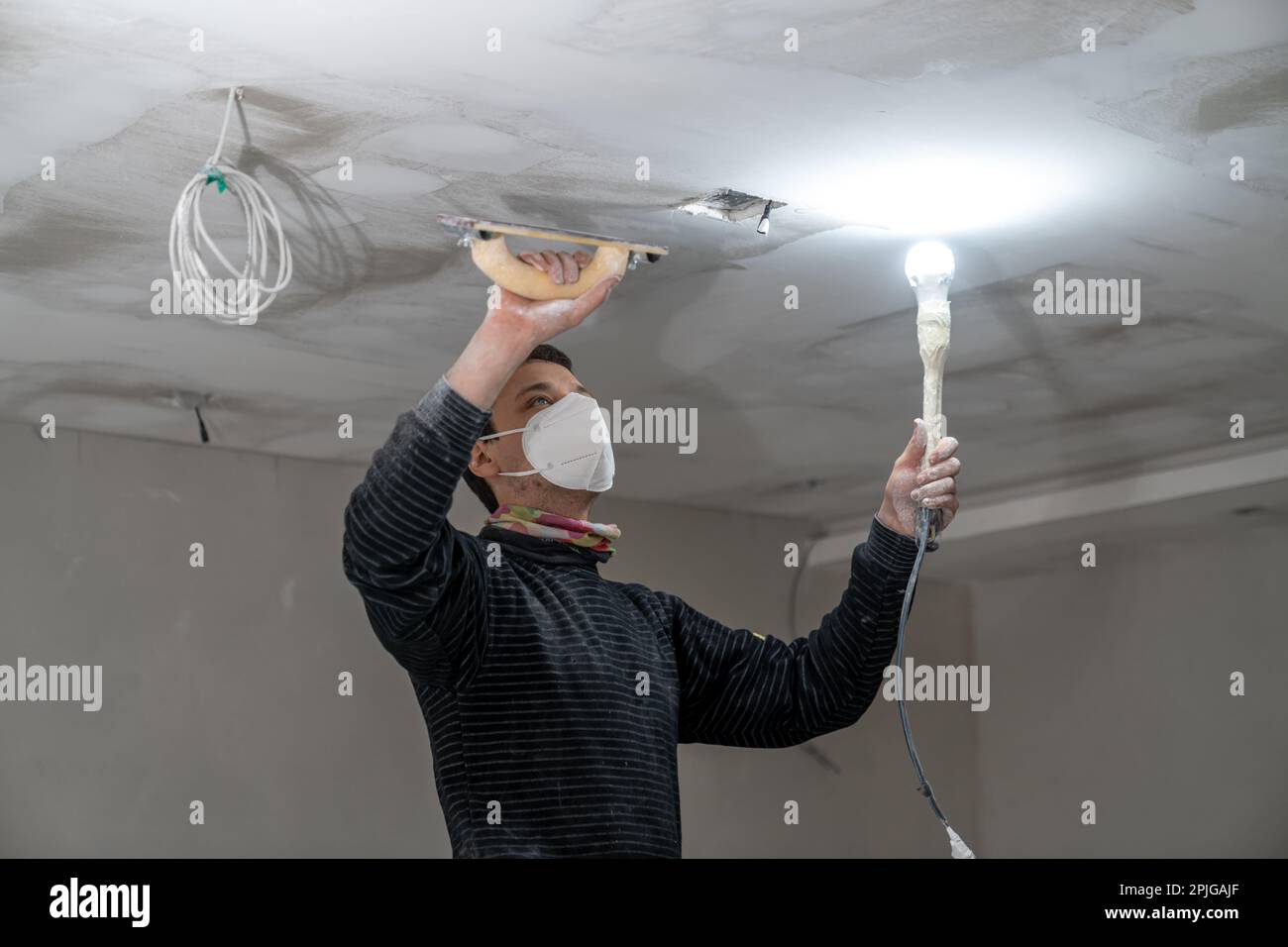 sanding a plasterboard ceiling in a new building with a trowel Stock