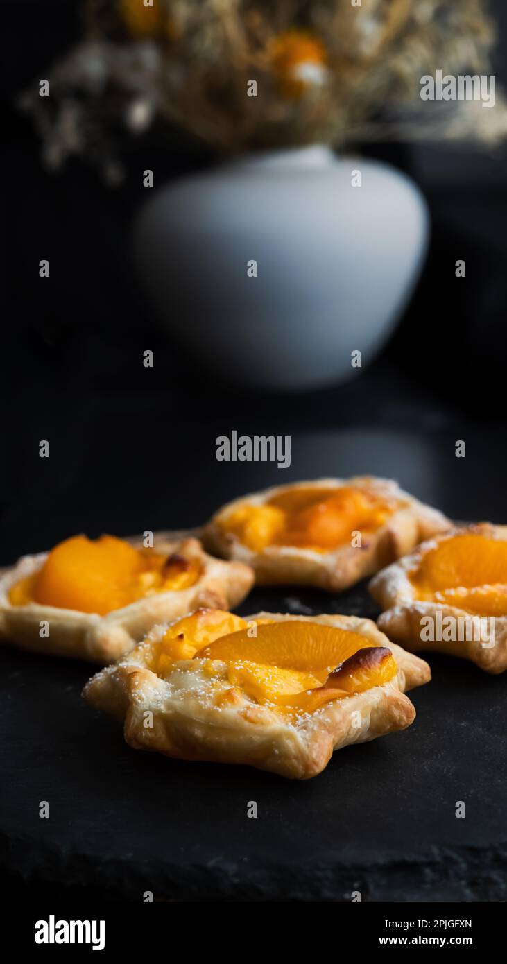 Puff pastry with custard, peach on round black slate, moody dark pictures with shallow depth of field. Front view. Stock Photo