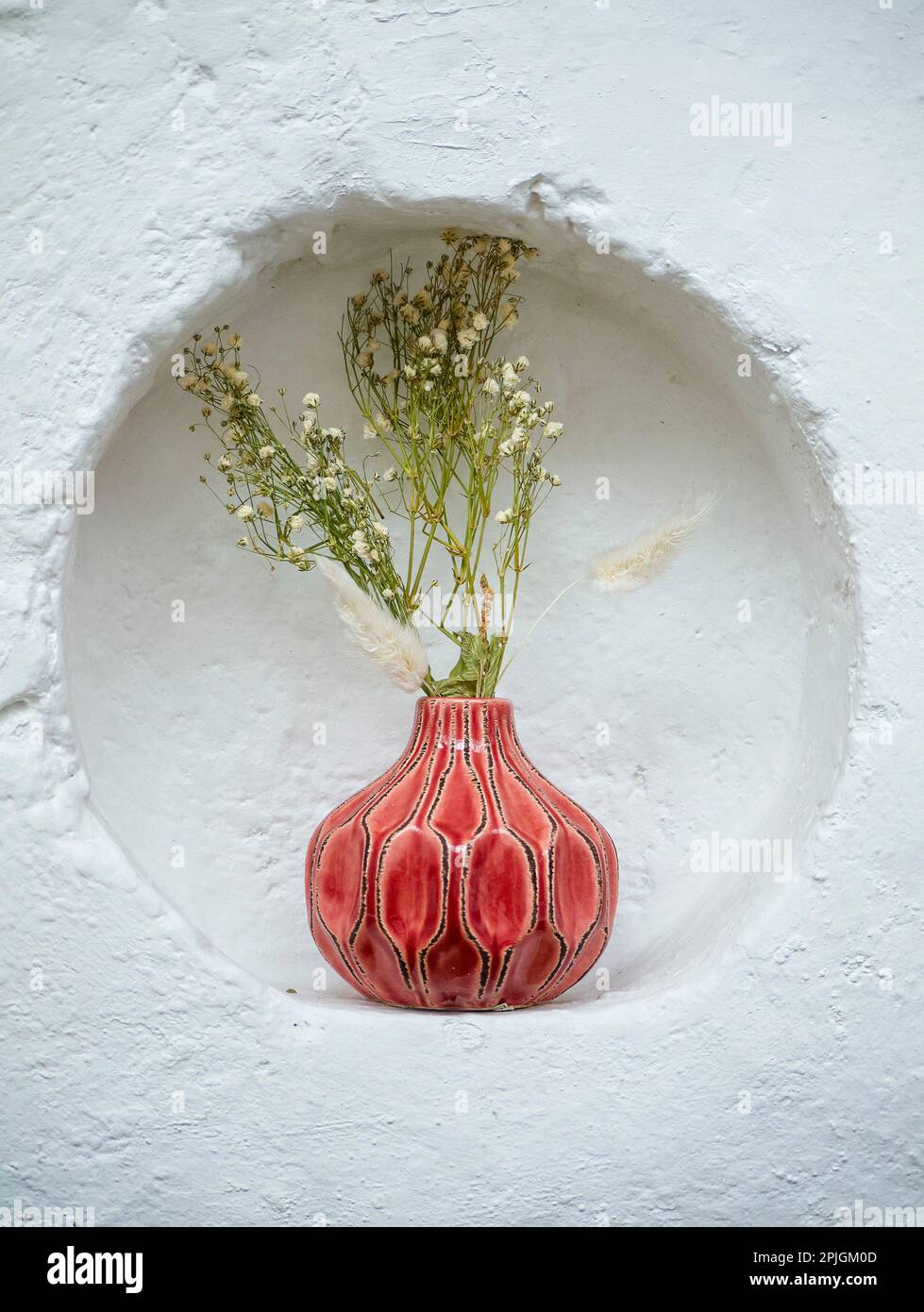 Wild flowers in a red vase, housed in a porthole against a white wall