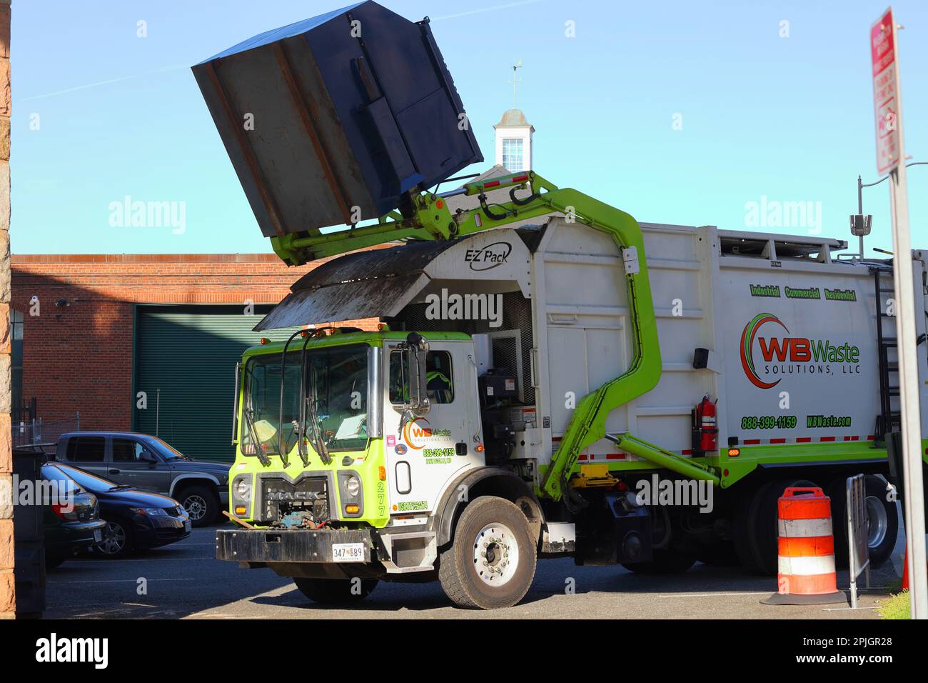 A WB Waste Solutions front load garbage truck with Hercules mechanism, EZ Pack body, and Mack Truck chassis lifts a 6 yd dumpster for trash removal. Stock Photo