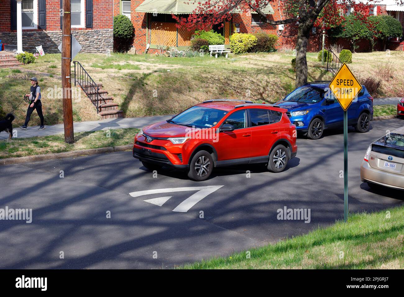 A red car goes over a speed bump, speed hump. Speed humps are designed to slow traffic speeds in low volumn roads, especially in residential Stock Photo