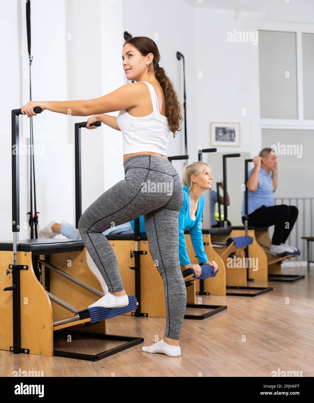 Smiling young European woman working on Pilates wanda chair machine with  standing exercises during wellness training Stock Photo - Alamy