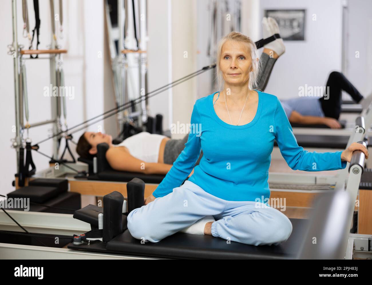 Senior female performing mermaid exercise on reformer Pilates machine