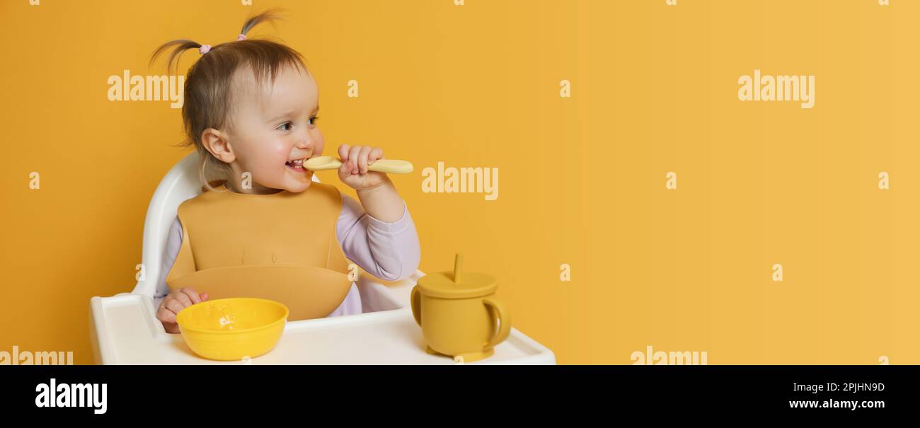 Cute little baby wearing bib while eating on yellow background, space ...