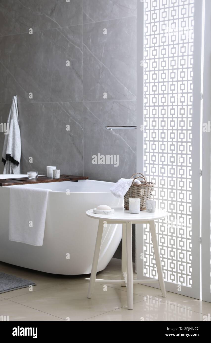 Modern white tub and table with toiletries in bathroom. Interior design