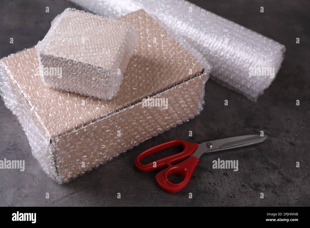Cardboard boxes, bubble wrap and scissors on dark grey table Stock Photo
