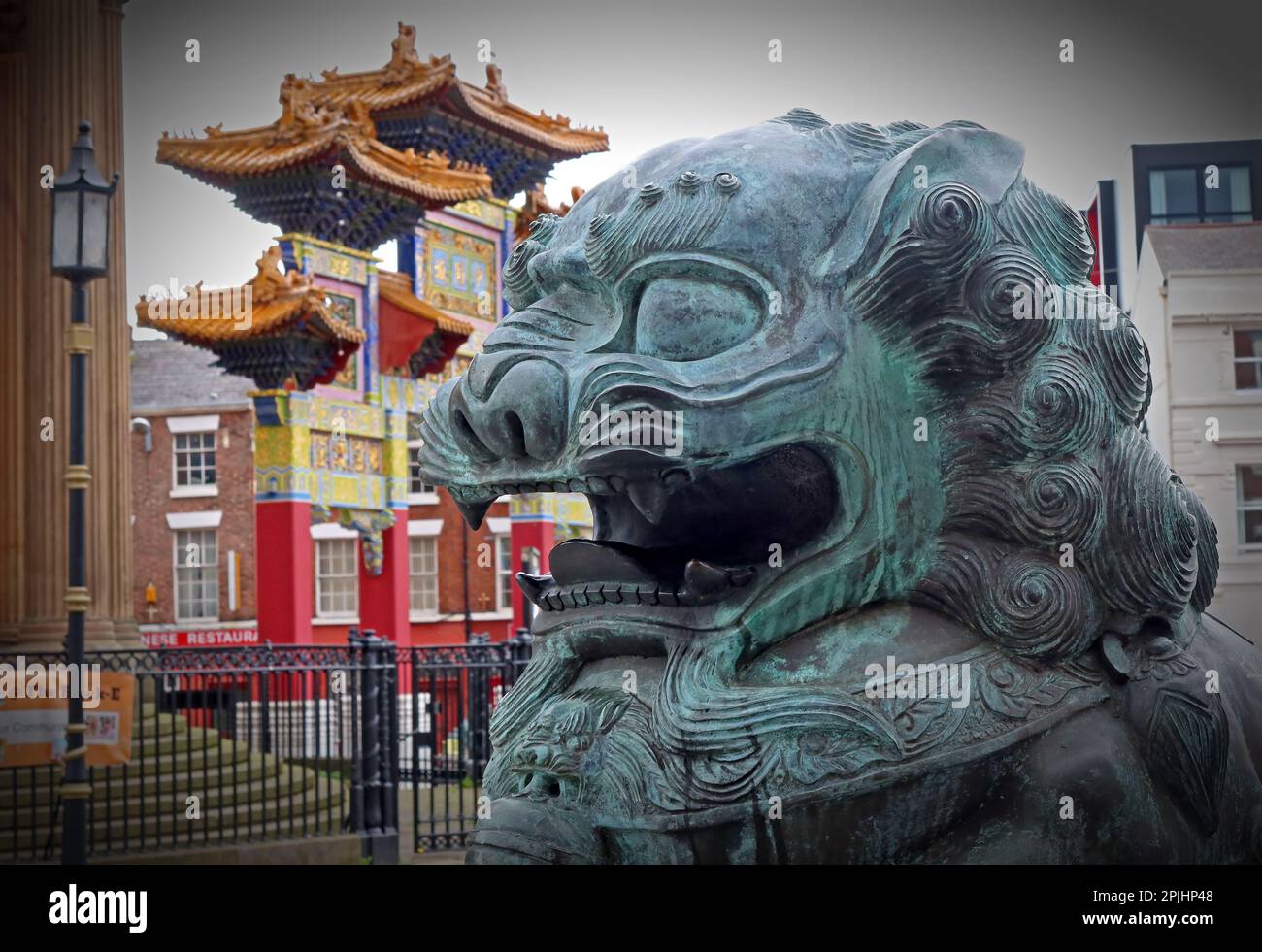 Chinese Guardian bronze Lion in front of The Paifang Chinatown Gate, Nelson Street, Liverpool, Merseyside, England, UK, L1 5DN Stock Photo
