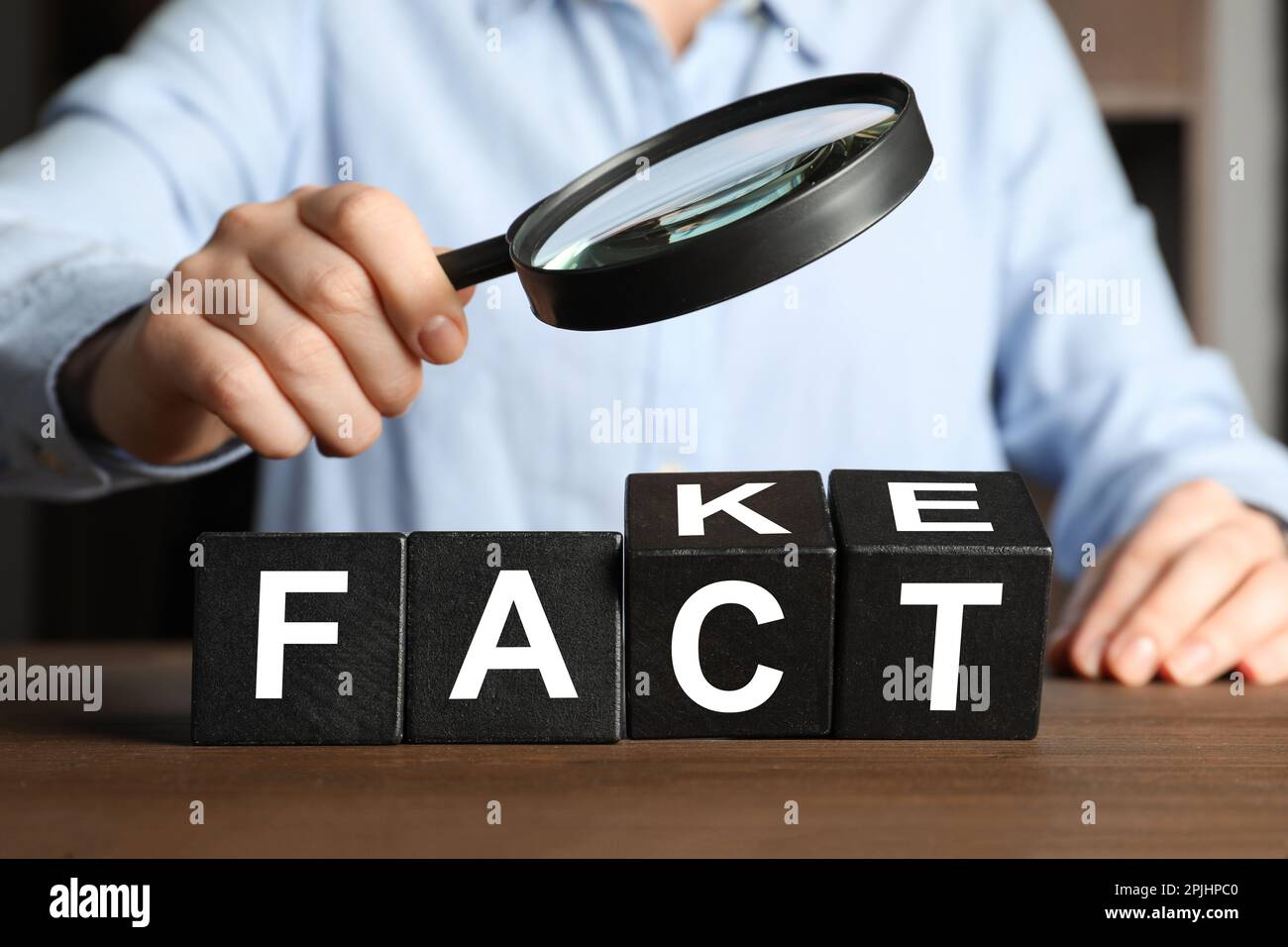 Woman holding magnifying glass above words FAKE and FACT made with ...