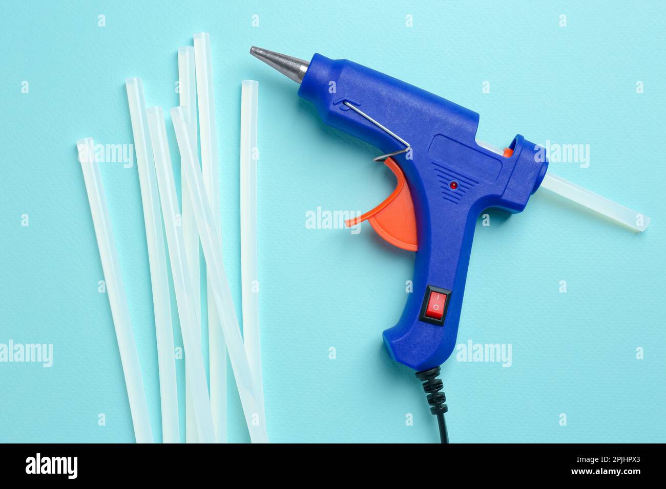 Blue glue gun and sticks on turquoise background, flat lay Stock Photo