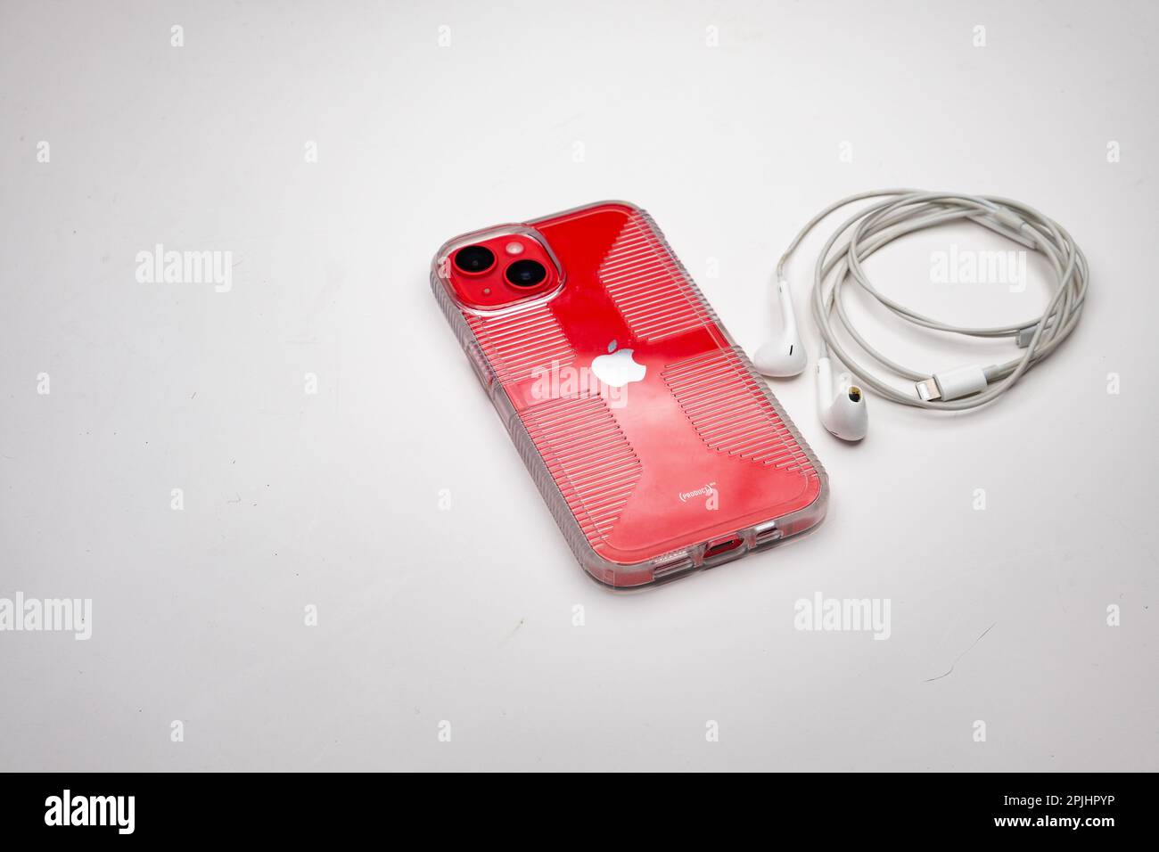 Apple iPhone 14 cellphone in (Product) Red color with earbuds and clear protective case on white background Stock Photo