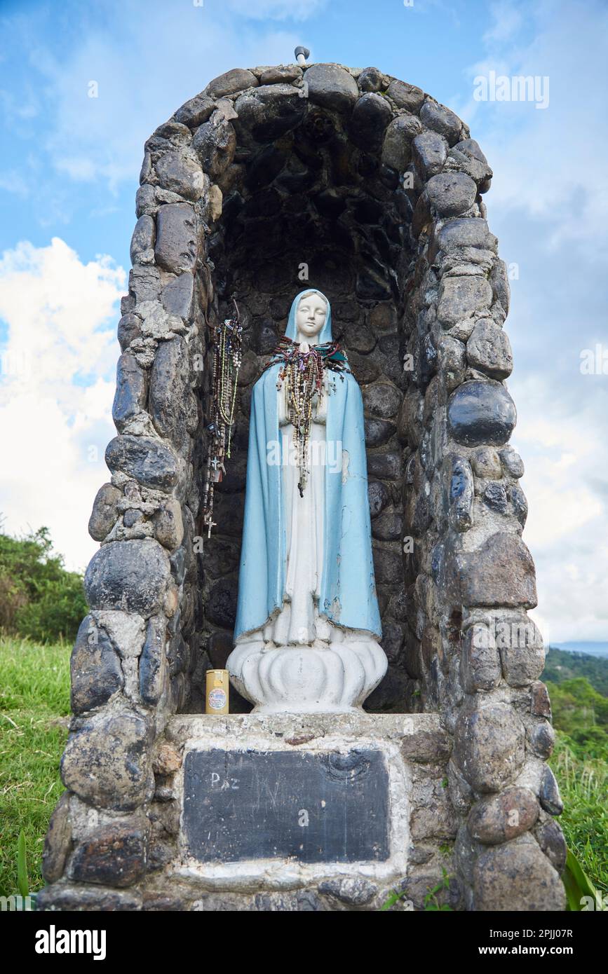 Nov 21, 2023, Puente Nacional, Santander, Colombia: Statue of the Virgin located outdoors with many rosaries hanging and protected in a stone niche. C Stock Photo