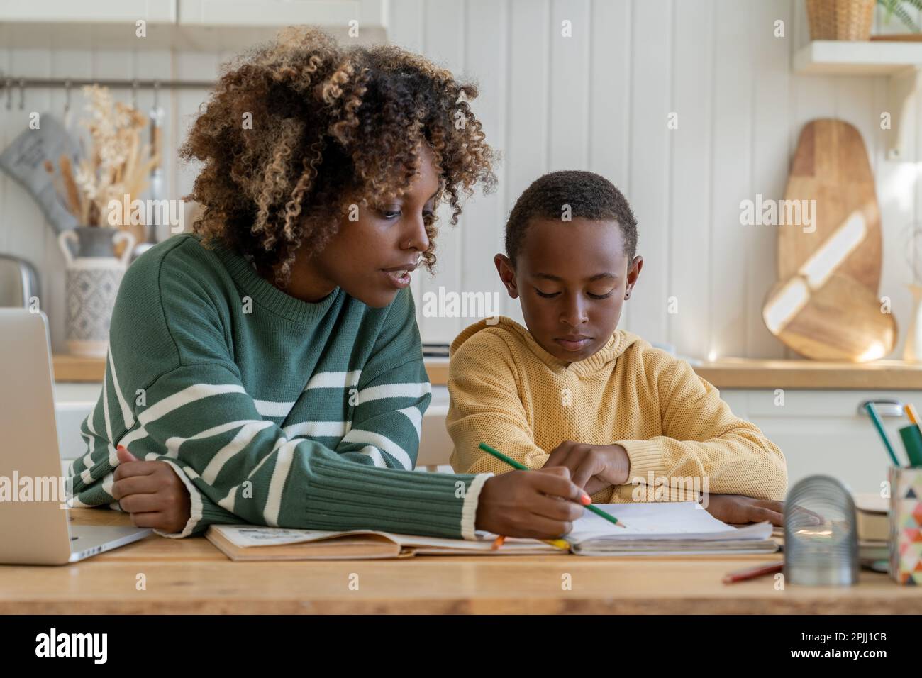 Homeschooling biracial pupil boy with help of personal tutor woman. Pensive son do homework with mom Stock Photo