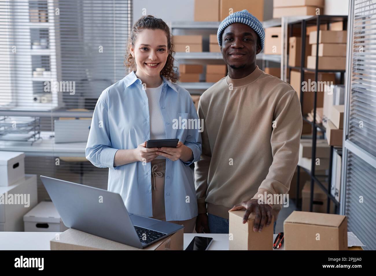 Happy young male and female managers of delivery center or storage room looking at camera with smiles while standing by workplace Stock Photo