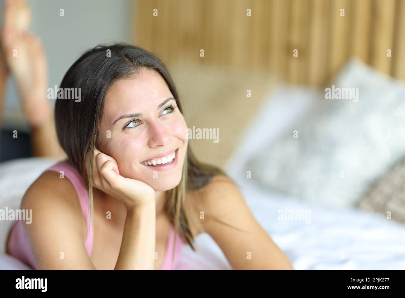 Happy teen thinking and looking at side on a bed at home Stock Photo