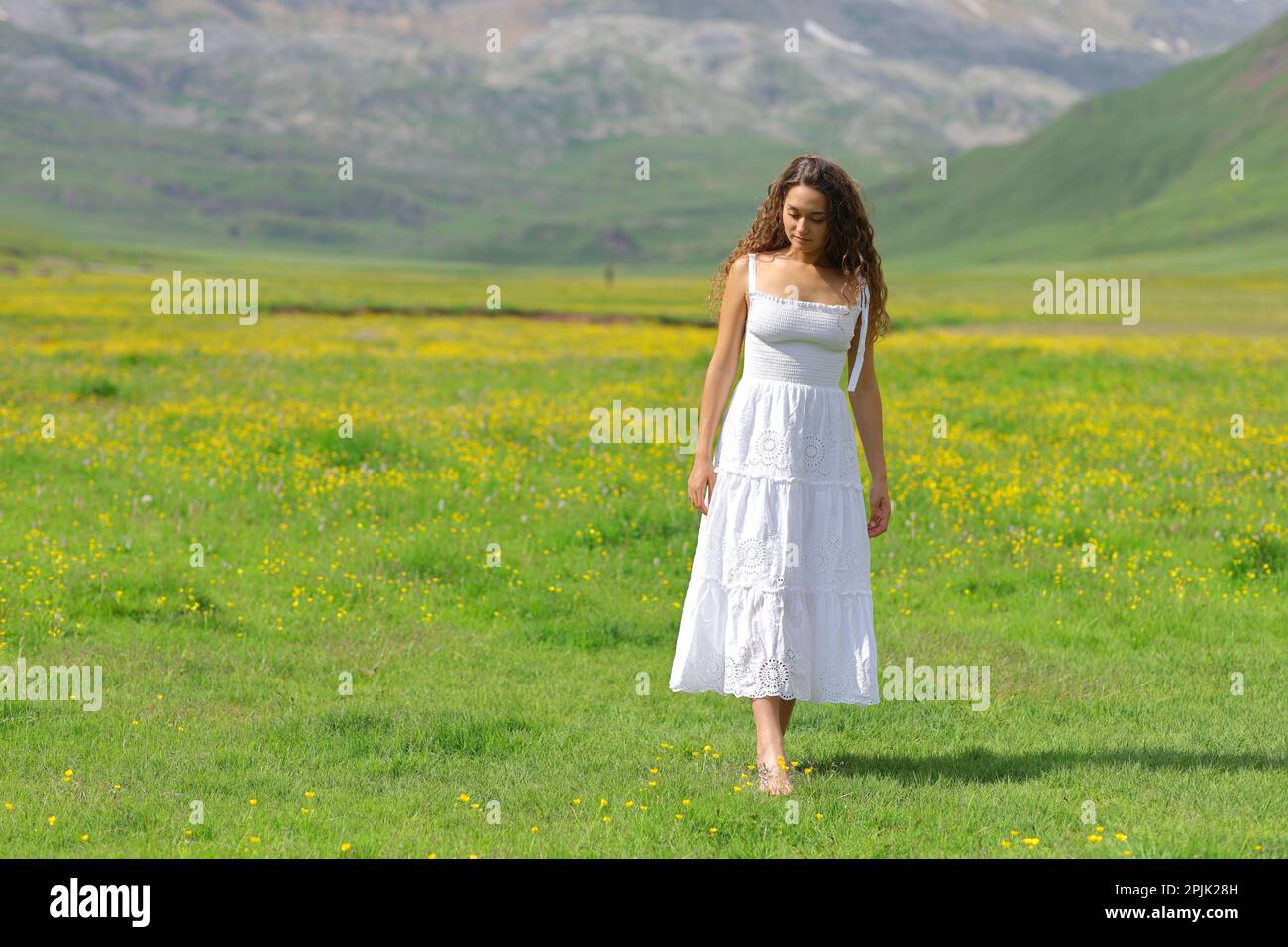 Woman in white dress walking barefoot on the grass in the mountain Stock Photo