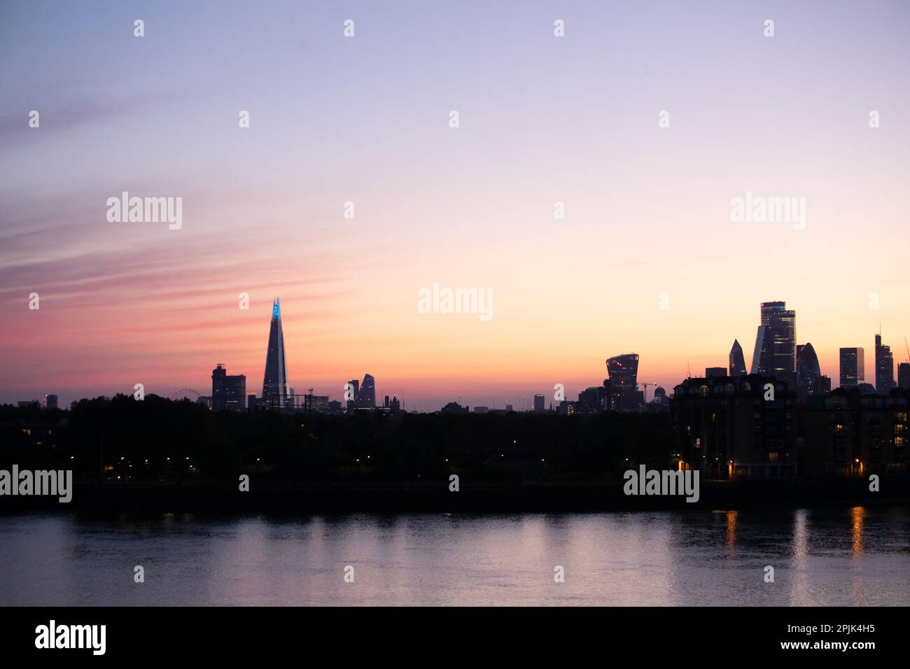 Pink, purple and orange striped radiatus altostratus clouds cover the sky over the London skyline at sunset. Stock Photo
