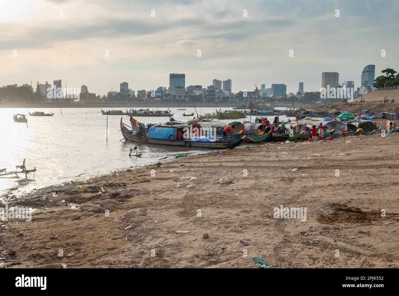 Small boats sit on muddy eastern bank of the river,much less developed than the riverside to the west.Setting sun reflecting on water,making silhouett Stock Photo