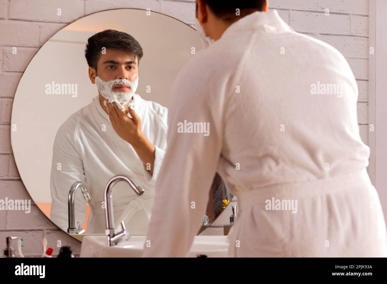 Young man applying shaving cream to his face in a bathroom at home Stock Photo