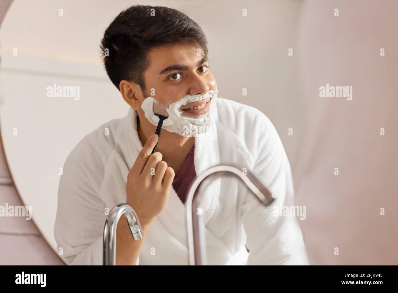 Young man shaving in front of bathroom mirror Stock Photo
