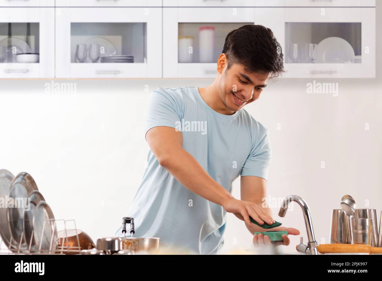 Cheerful man washing utensils with dish wash bar in kitchen at home Stock Photo