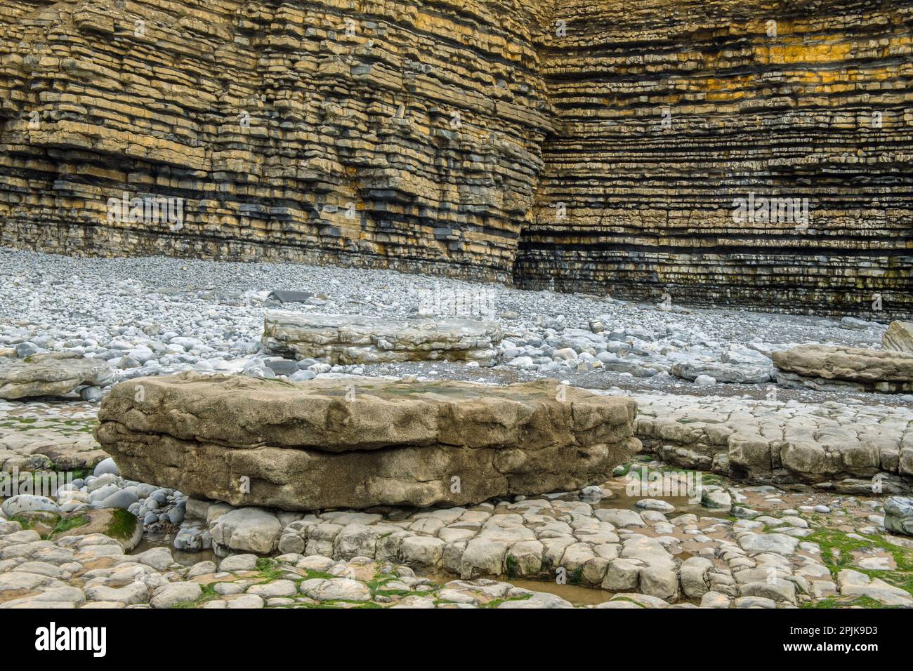 Limestone Cliffs in layers with rocka and pebbles below on Dunraven Bay on agrey April afternoon on the Vale of Glamorgan and Glamorgan Heritage Coast Stock Photo