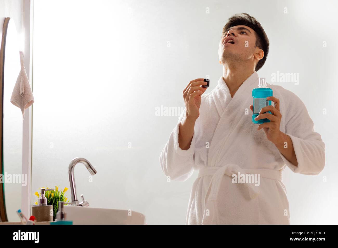 Young man gargling with mouthwash in bathroom Stock Photo