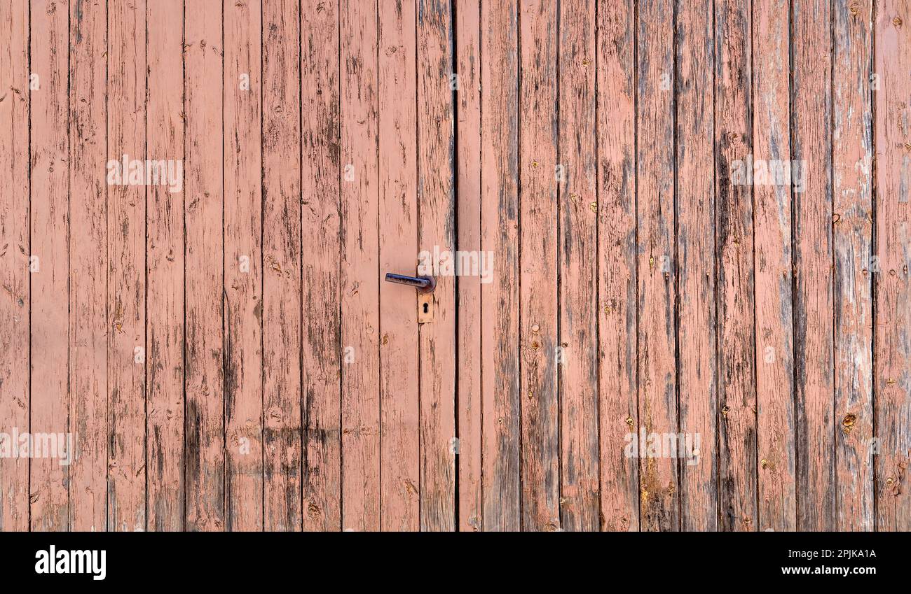 Old double wing wooden garage door with heavily weathered paint Stock Photo