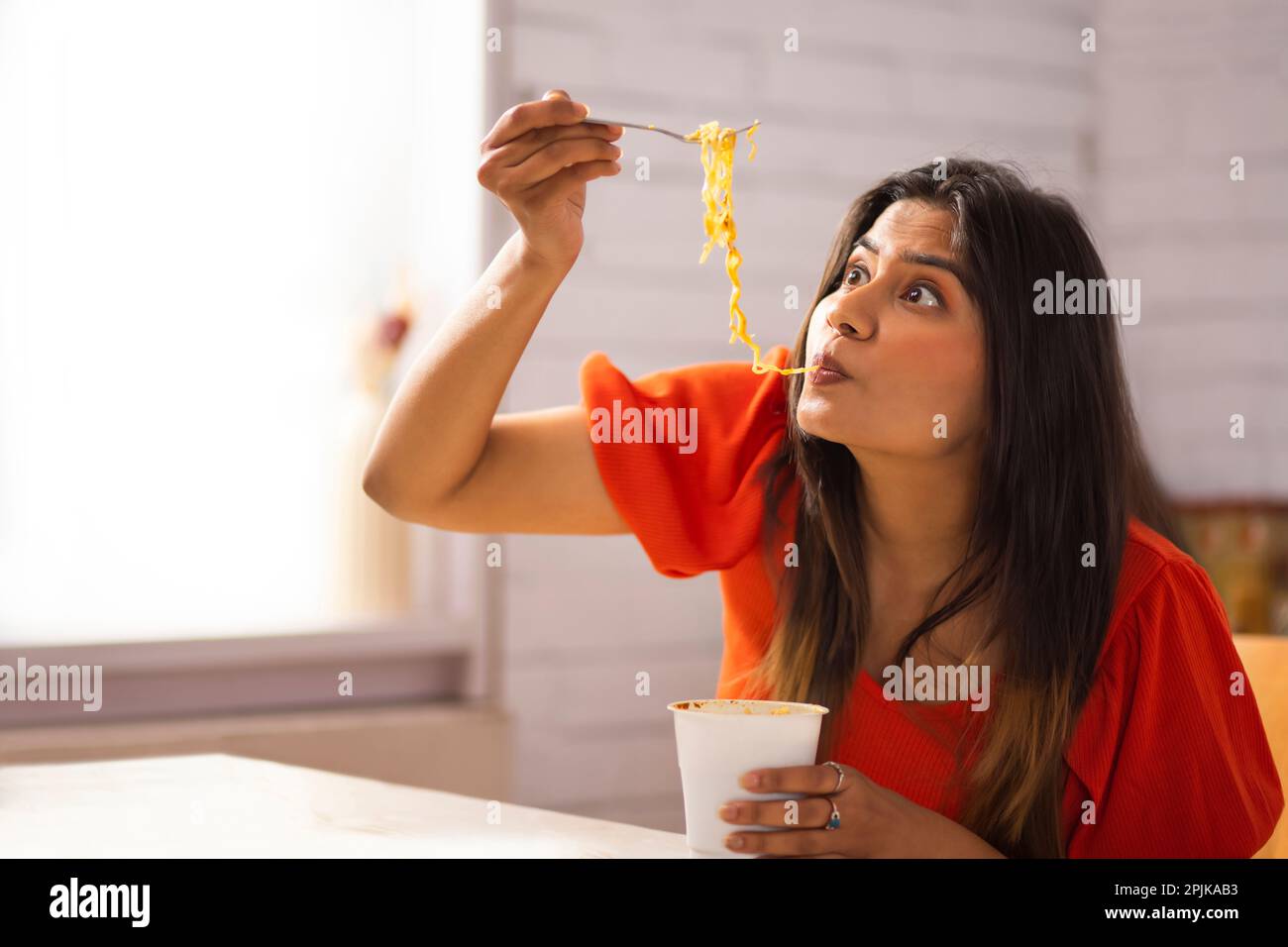 Portrait of woman eating noodles in kitchen Stock Photo