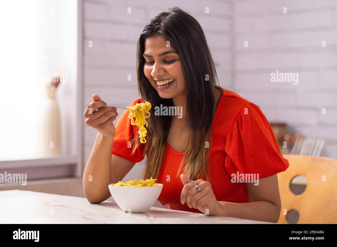 Portrait of woman eating noodles in kitchen Stock Photo