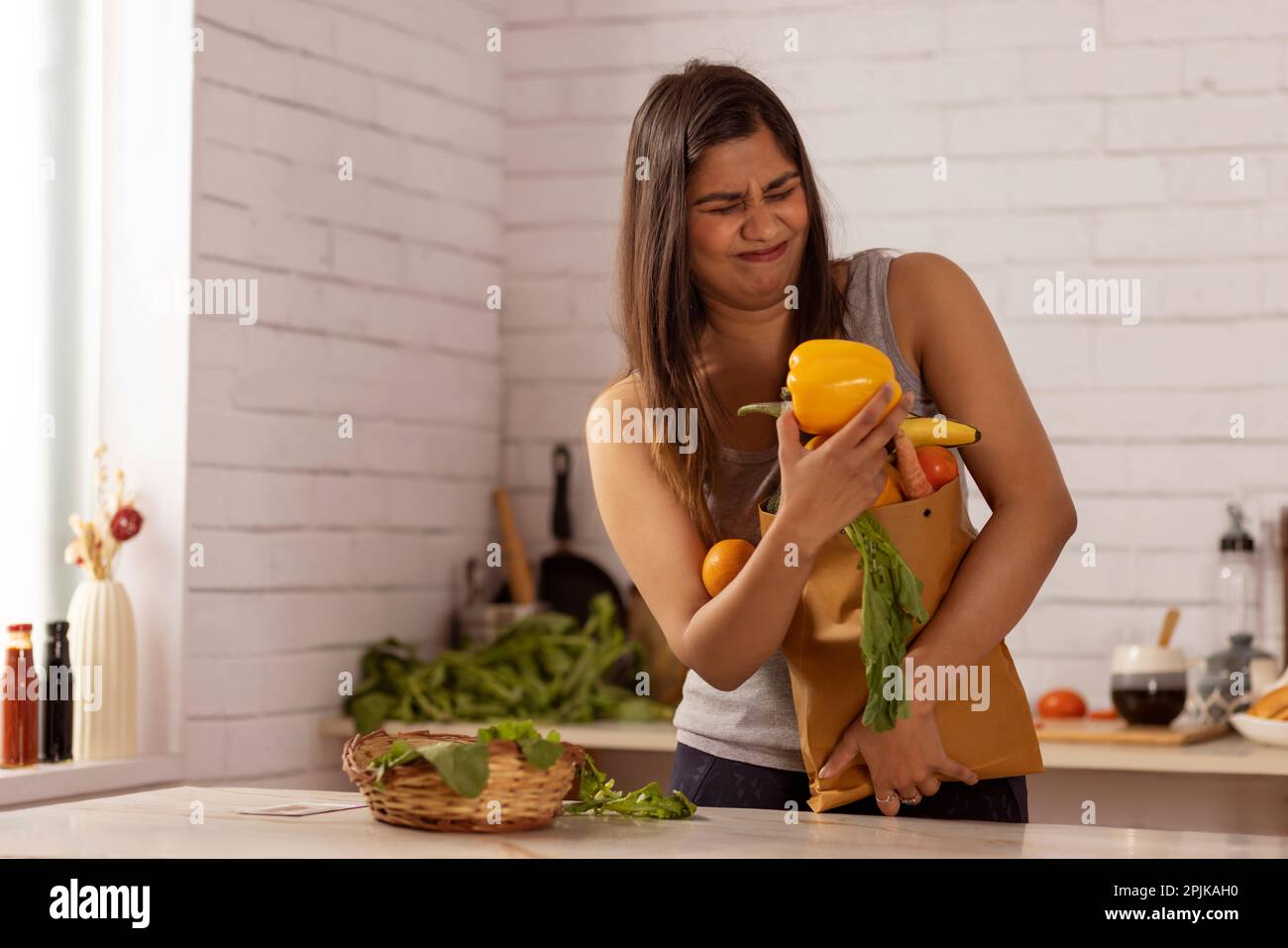 Woman standing in kitchen holding a heavy bag of vegetables Stock Photo