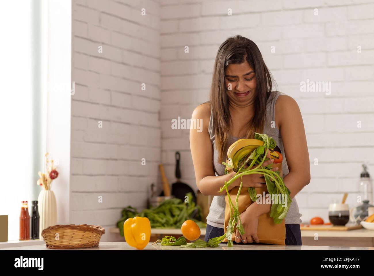 Woman standing in kitchen holding a heavy bag of vegetables Stock Photo