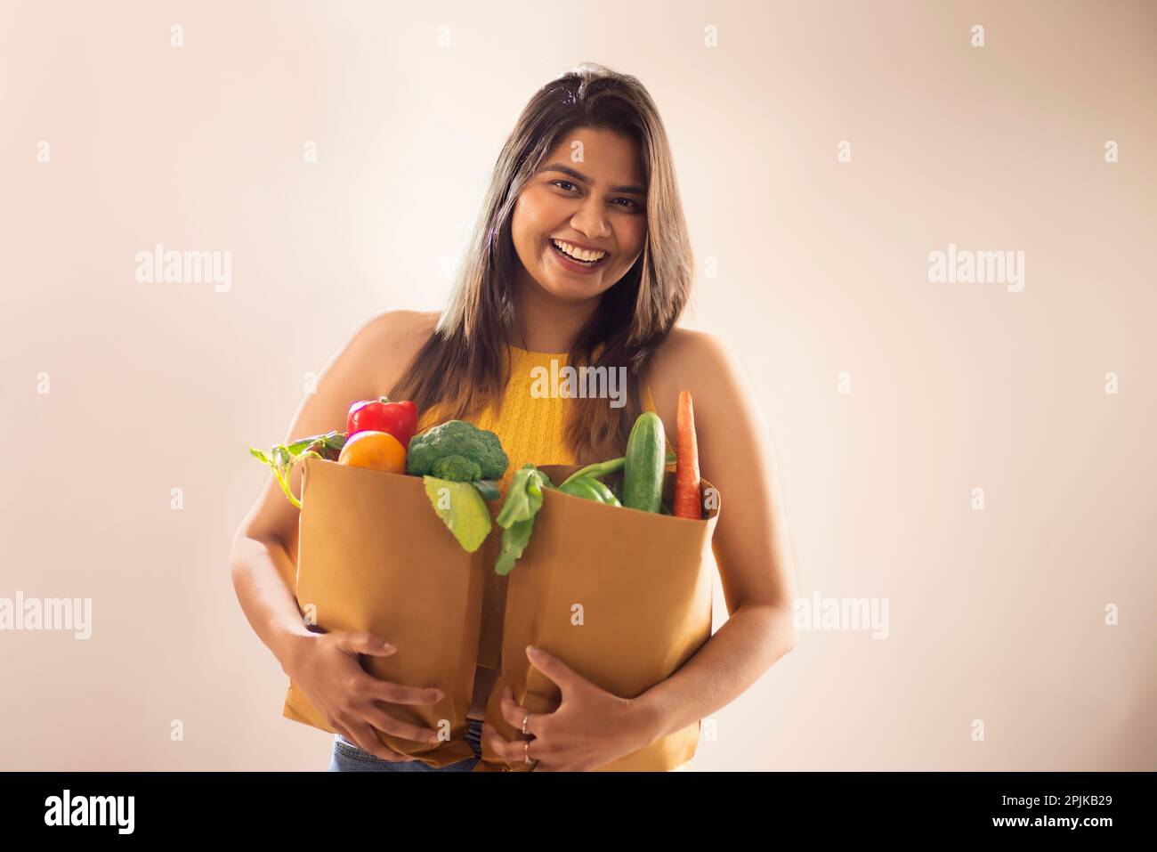 Smiling woman holding bags of fresh vegetables and fruits against white background Stock Photo
