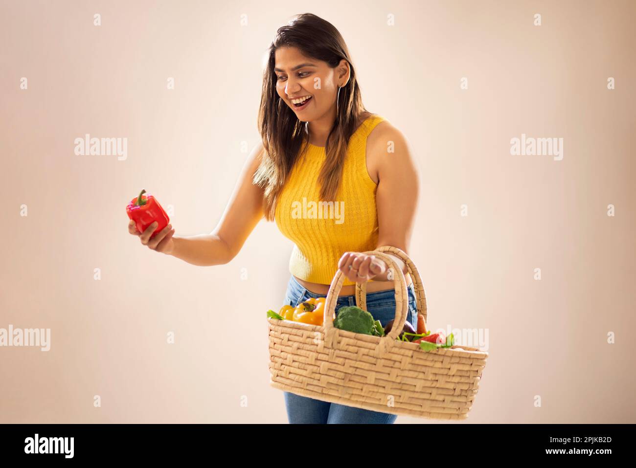Smiling woman holding a basket of fresh vegetables and red bell pepper ...