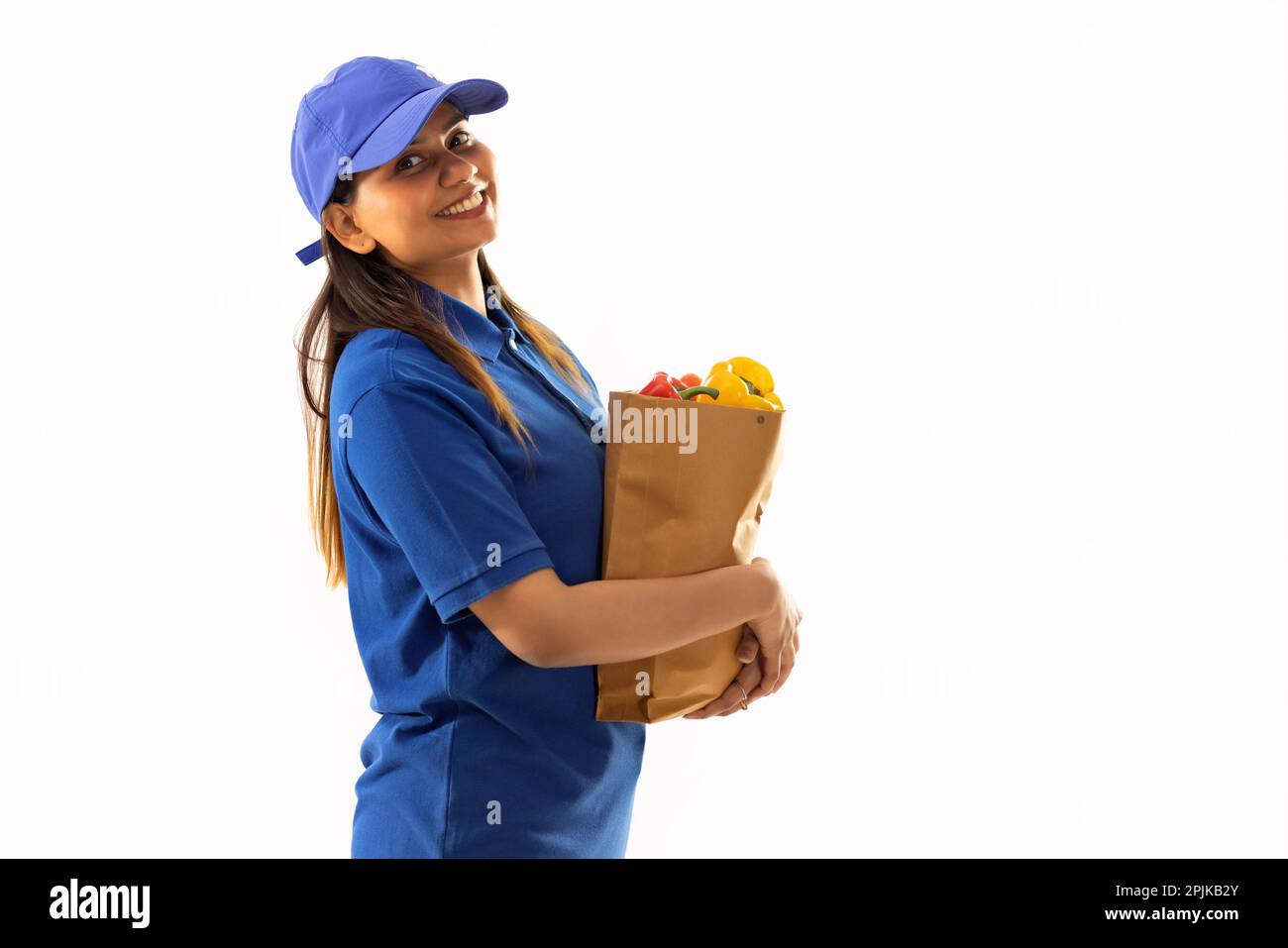 Side view of delivery woman holding a bag of fresh vegetable against white background Stock Photo