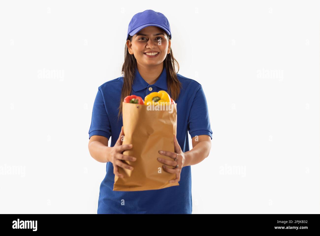 Portrait of delivery woman holding a bag of fresh vegetable against white background Stock Photo