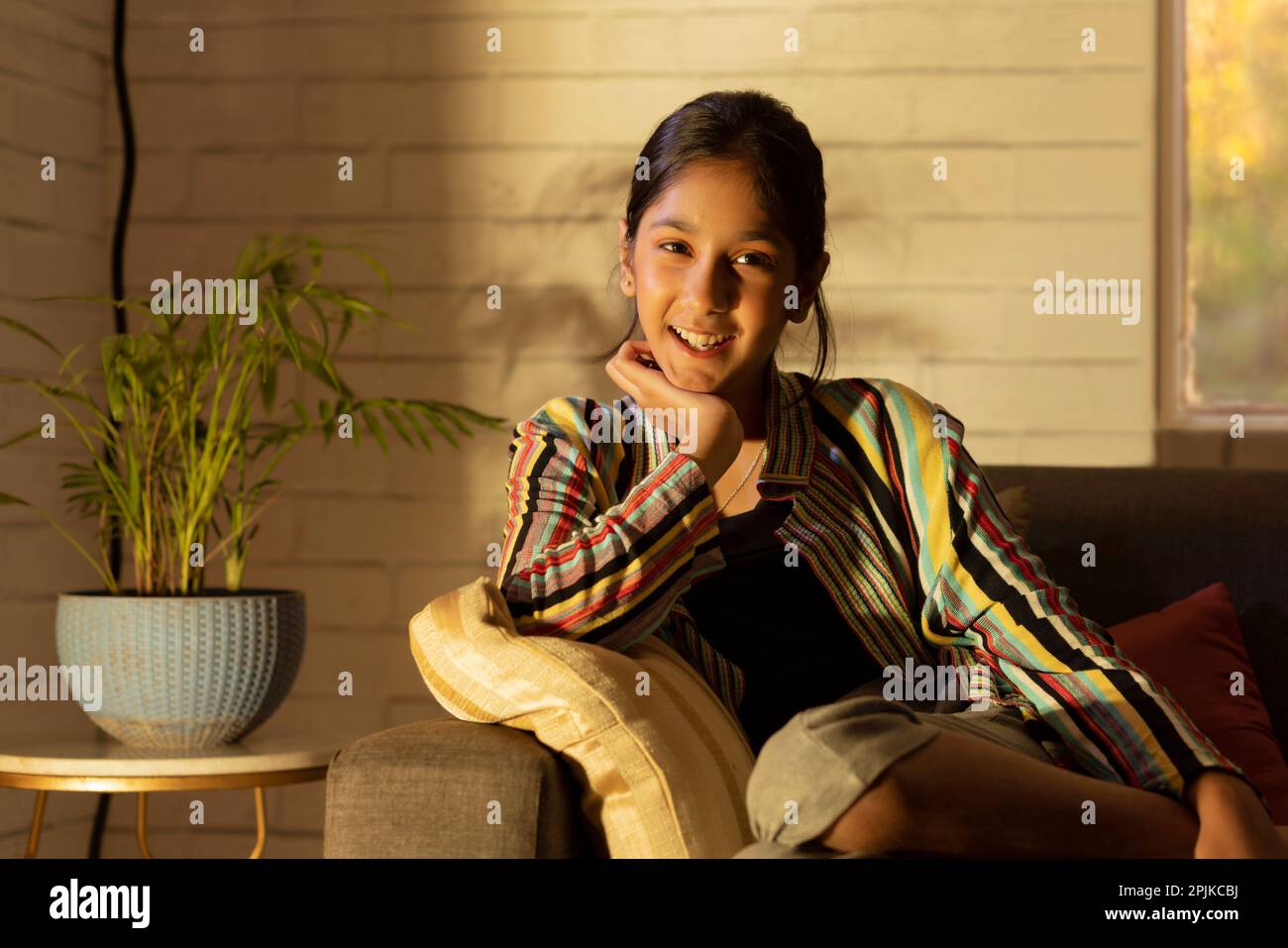 Portrait of a cheerful girl sitting on sofa and looking at camera Stock ...