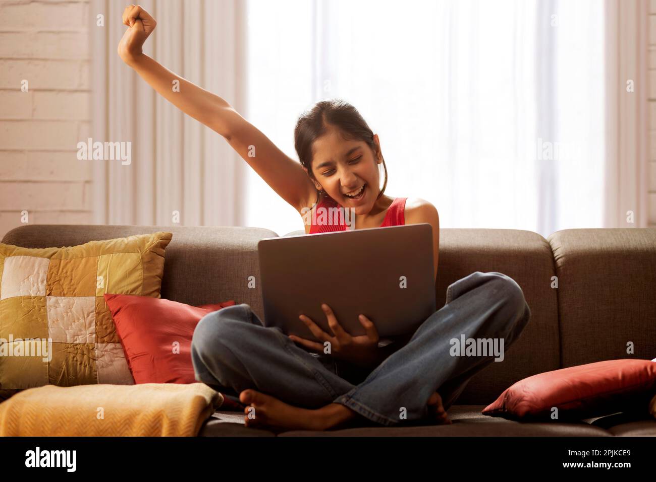 Excited girl cheering while watching video on laptop in living room Stock Photo