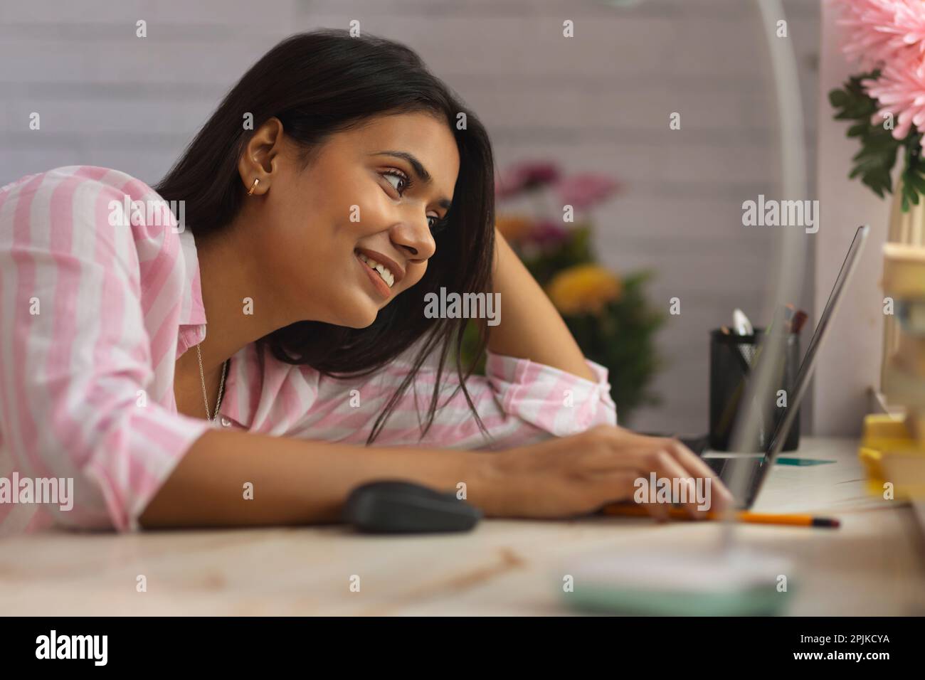 Close-up portrait of a young woman leaning on desk and using laptop Stock Photo