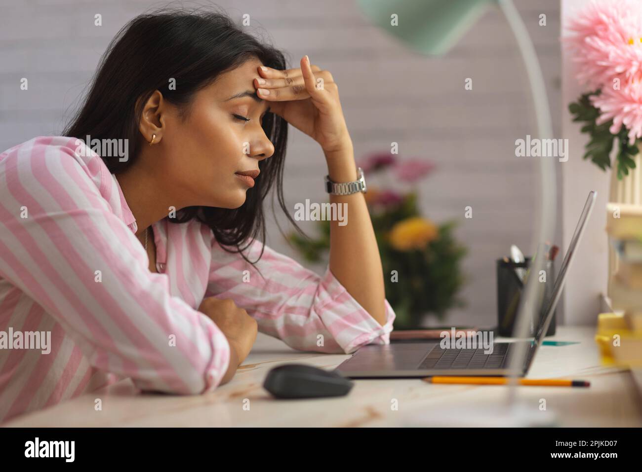 Close-up portrait of a tired woman sitting on desk with hand on head Stock Photo
