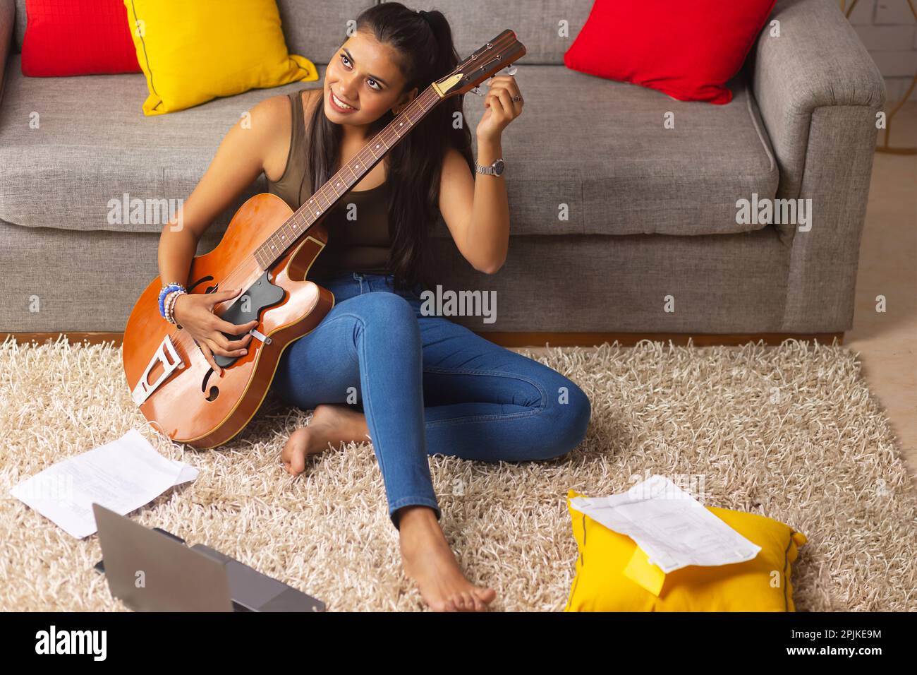 Young woman tuning guitar while sitting on floor in living room Stock Photo