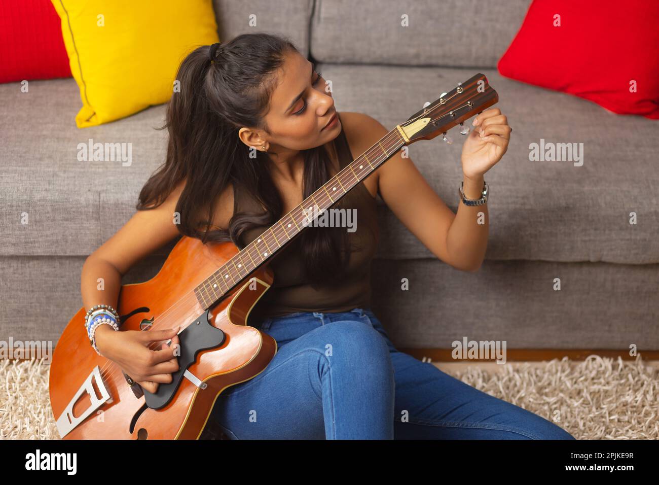 Young woman tuning guitar while sitting in living room Stock Photo