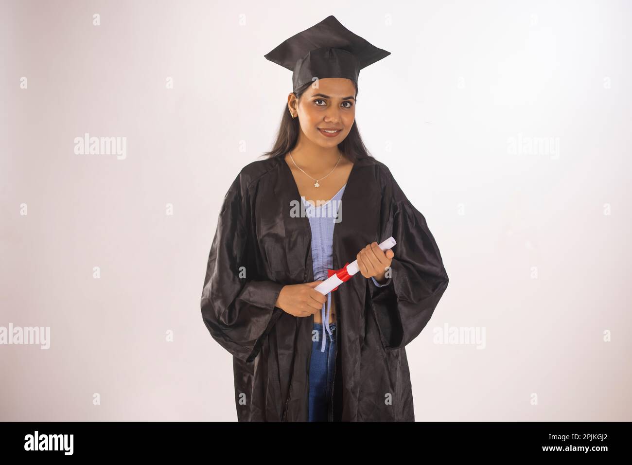 Portrait of graduate teen latin boy student in black graduation gown with  hat, holding diploma - isolated on background. Child back to school and  educational concept. Stock Photo