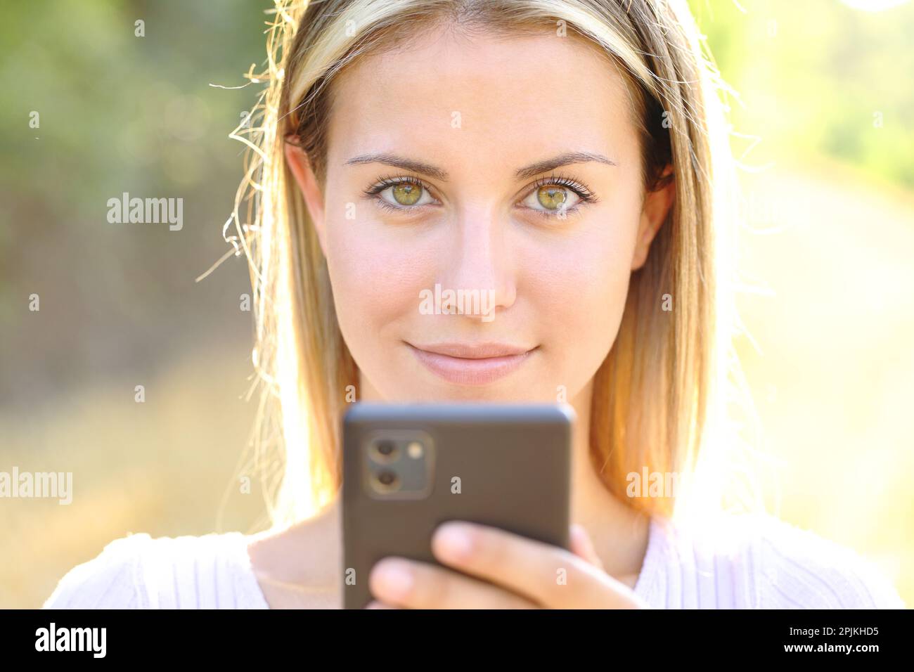 Front view portrait of a beautiful woman holding phone looking at camera outdoors Stock Photo