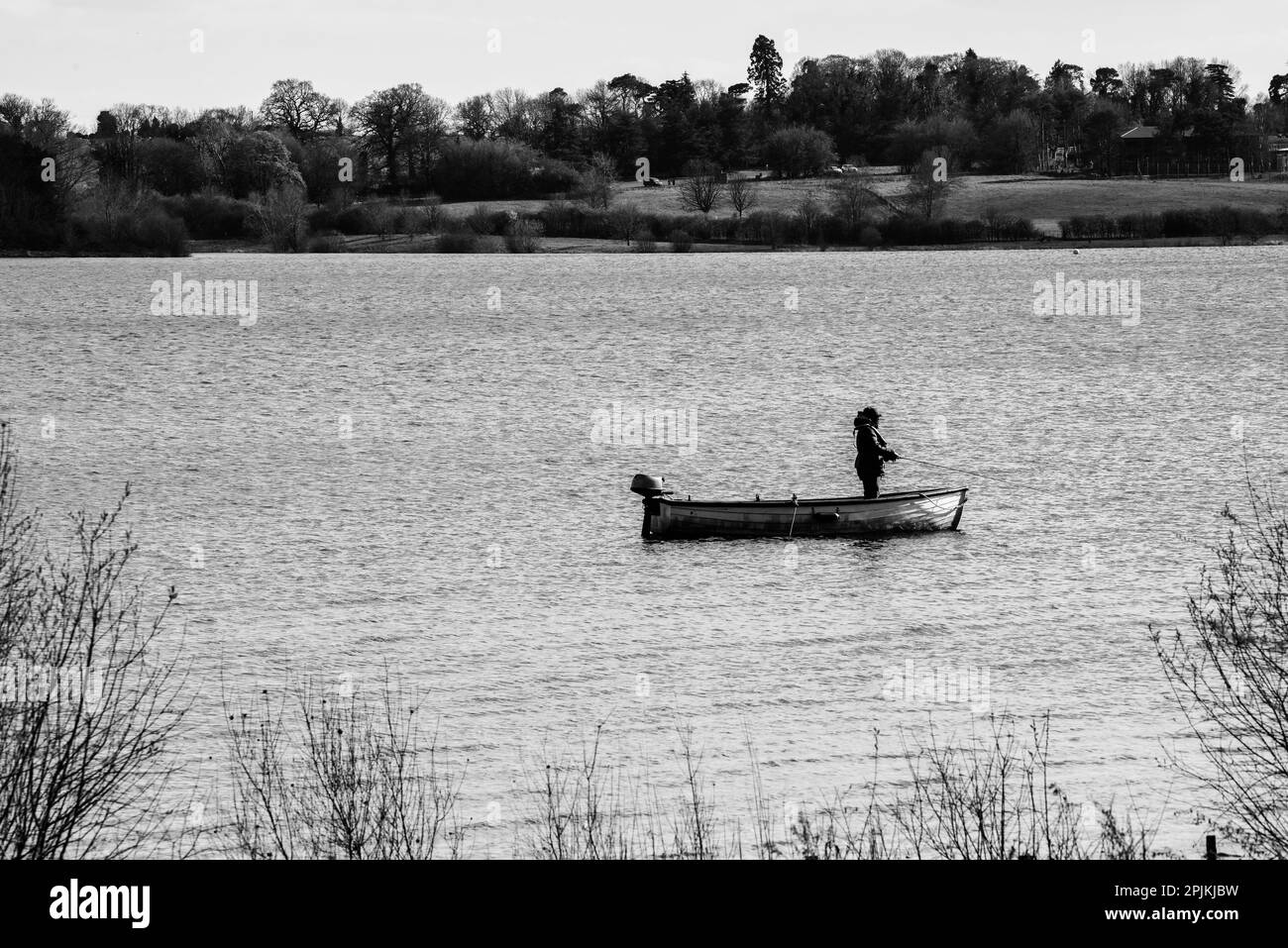 One man is alone fishing from a boat on a quiet lake Stock Photo