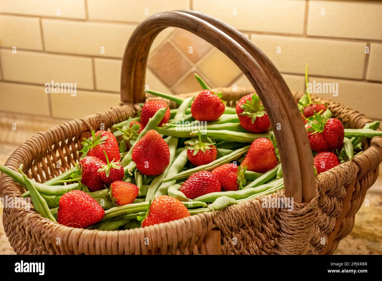 Issaquah, Washington State, USA. Woven basket of freshly harvested green beans and strawberries sitting on a granite kitchen countertop. Stock Photo