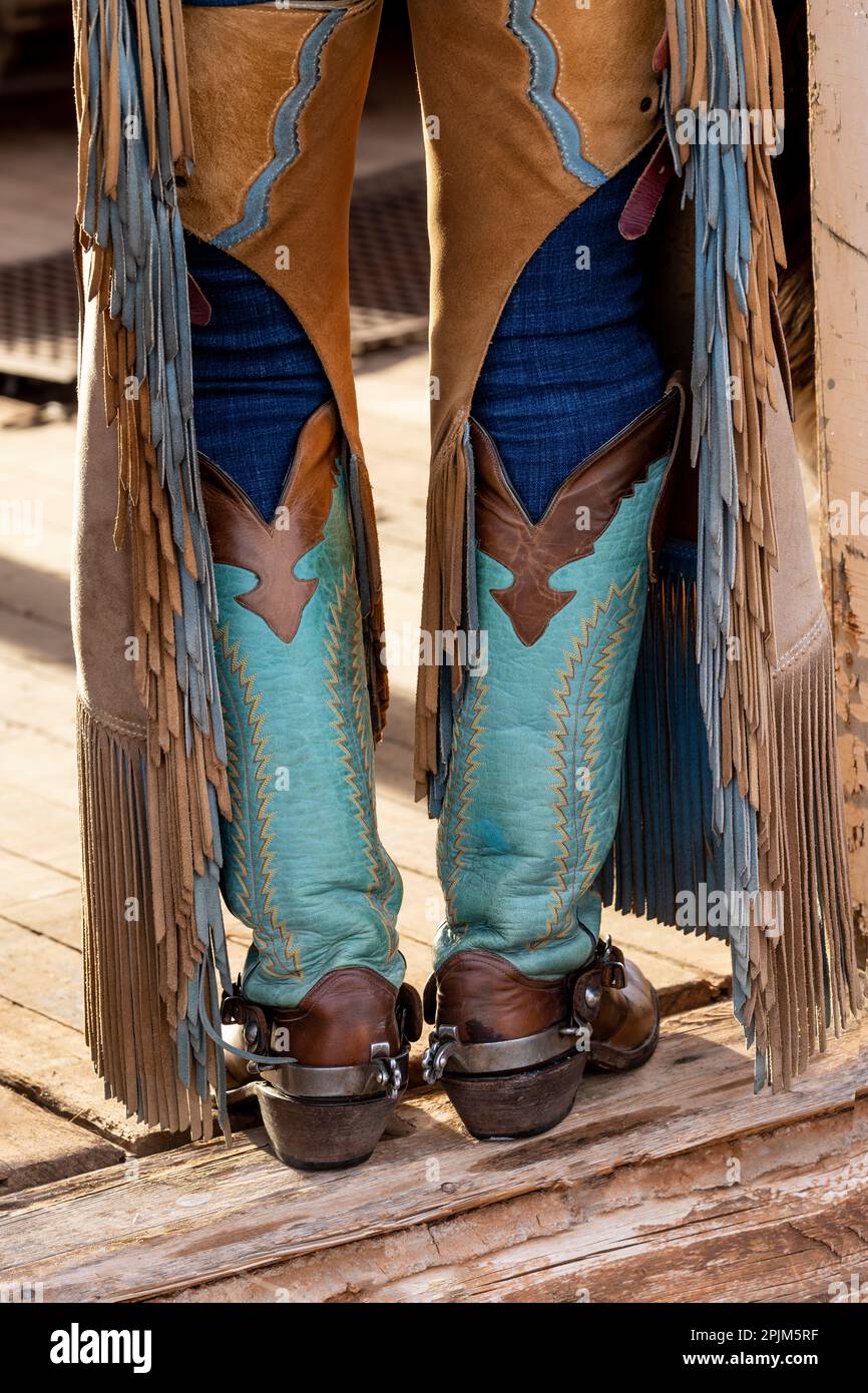 USA, Shell, Wyoming. Hideout Ranch cowgirl standing in doorway with cowboy boots and chaps. (PR,MR) Stock Photo