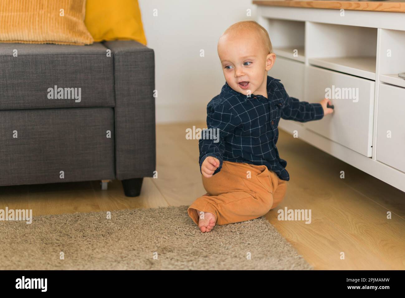 Toddler baby boy open cabinet drawer with his hand. Child explore what is in cabinet. Baby curiosity and child development stages Stock Photo